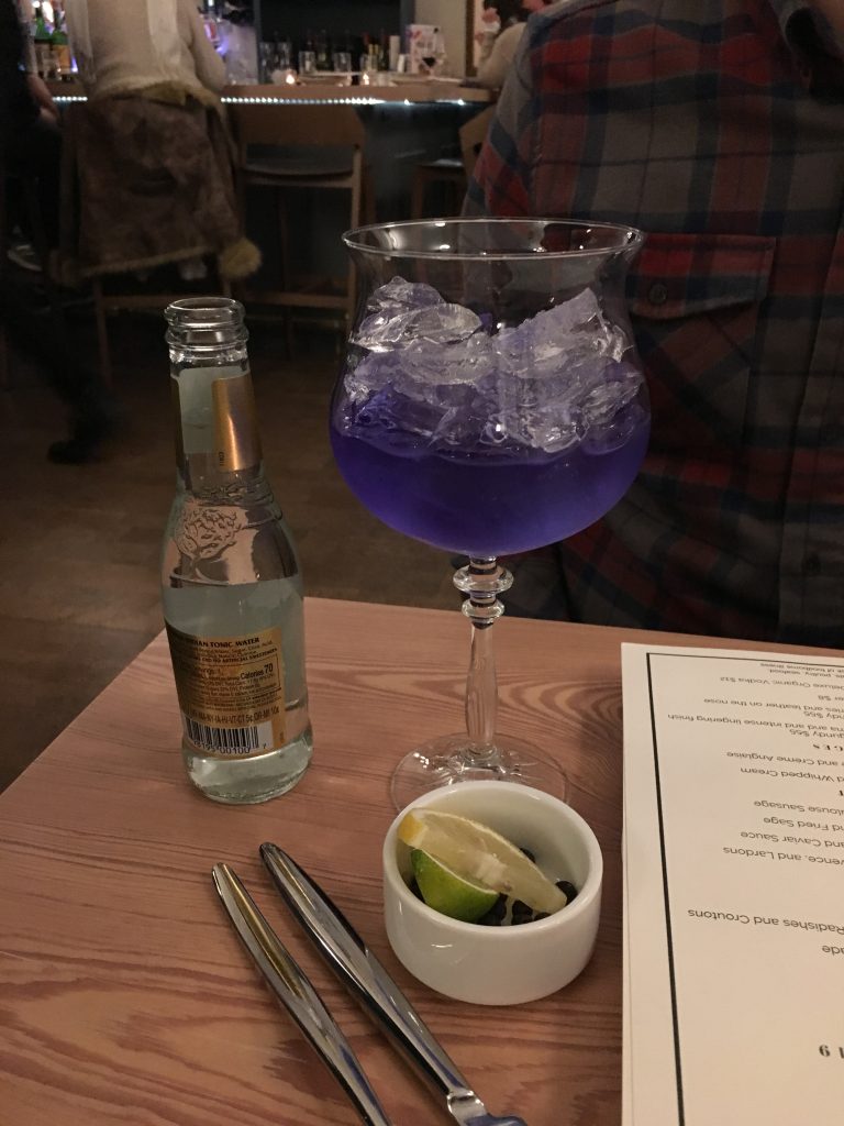 A cocktail with a purple liquid in a wine glass full of ice.