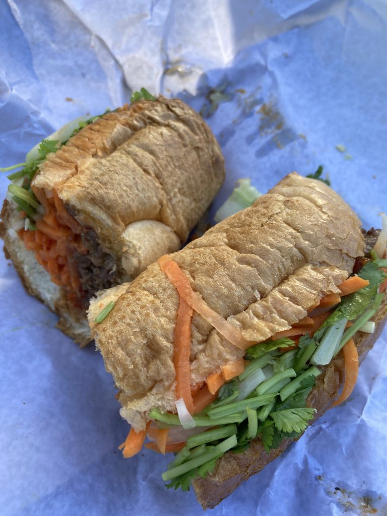 A banh mi sandwich on a baguette with meat, pickled carrots, and lots of fresh herbs.