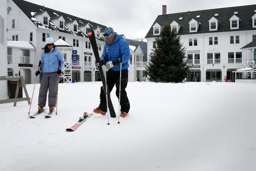 A couple putting their cross-country skis on in a courtyard of a resort.
