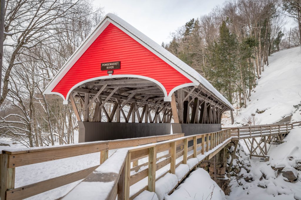 The bright red covered bridge in the Flume Gorge, surrounded by snow.
