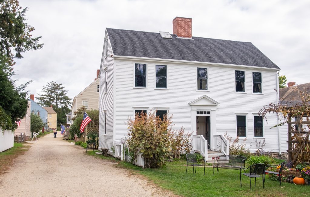 A white historic home from the 1700s with an American flag hanging next to it.
