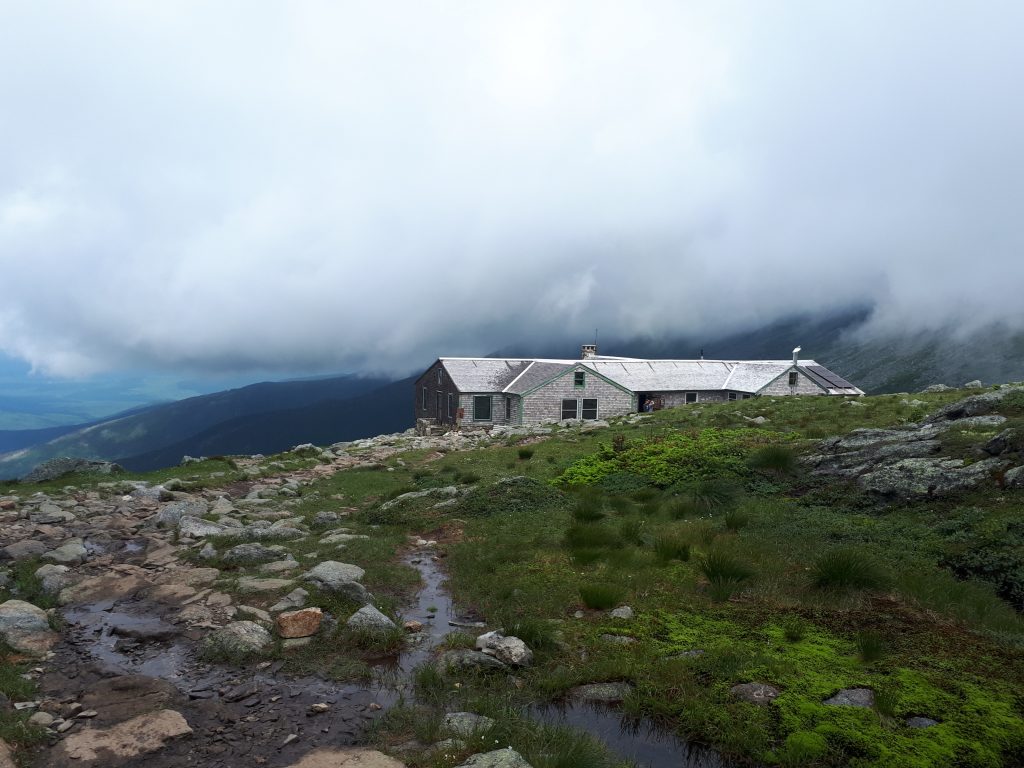 A small gray mountain hut perched among the clouds on the mountain.