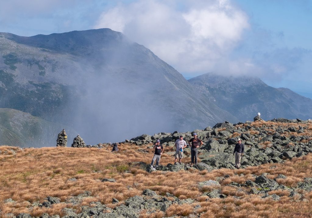 A group of hikers standing on a rocky trail in front of a mountain underneath a cloud-filled blue sky.