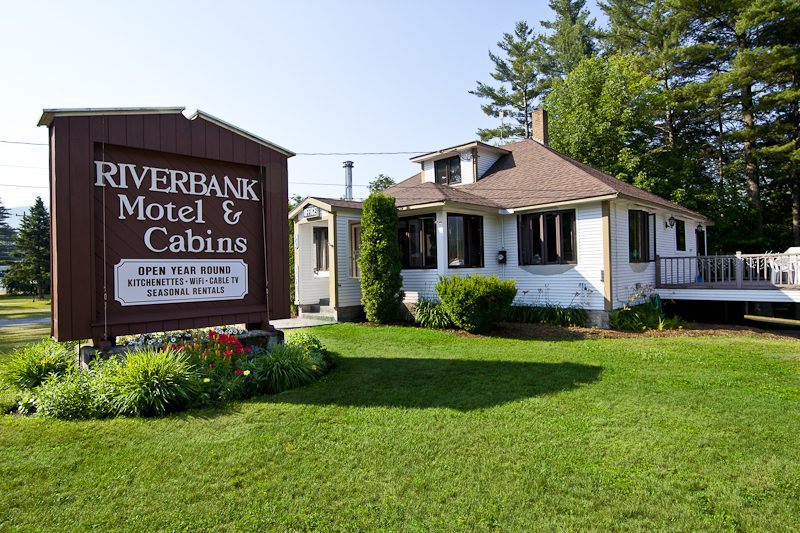 The sign for Riverbank Motel and Cabins, in front of a white cabin building