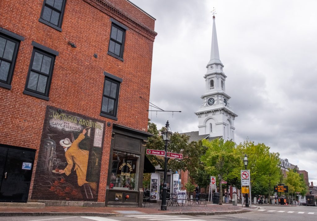 Market Square in Portsmouth, with a big white steepled church in the center and a mural of a man in a red fedora on one of the red brick walls.