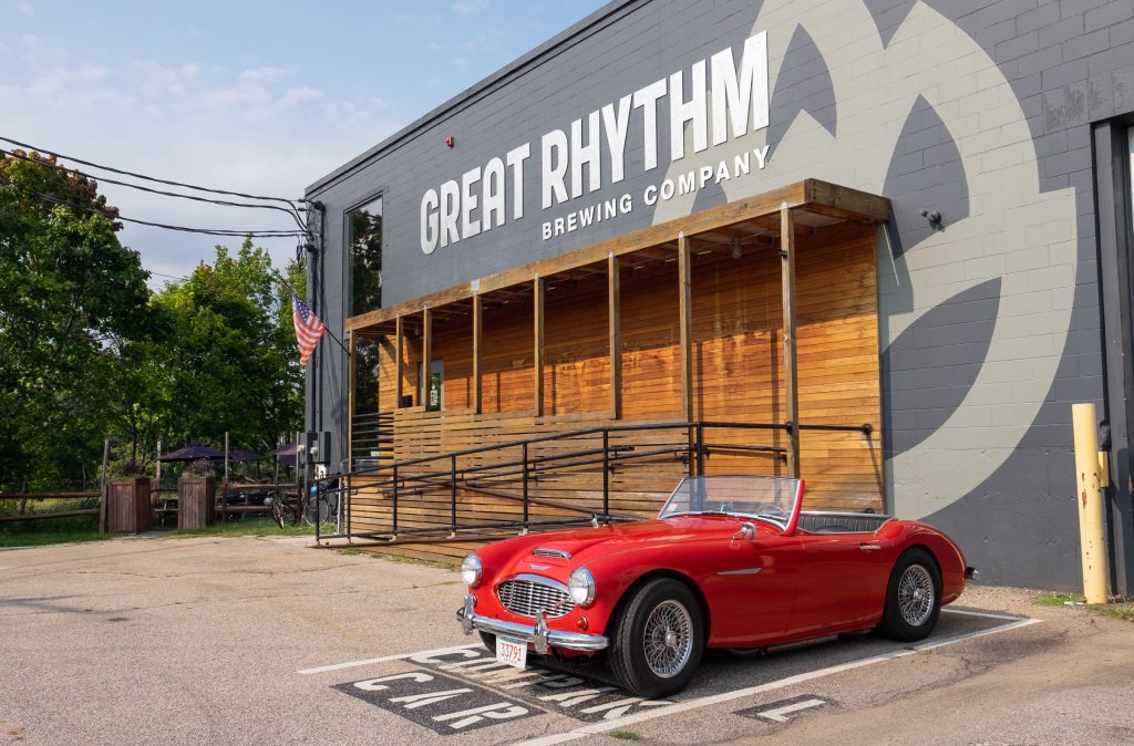 Great Rhythm Brewery, an industrial looking gray painted wall with a red vintage convertible parked out front.