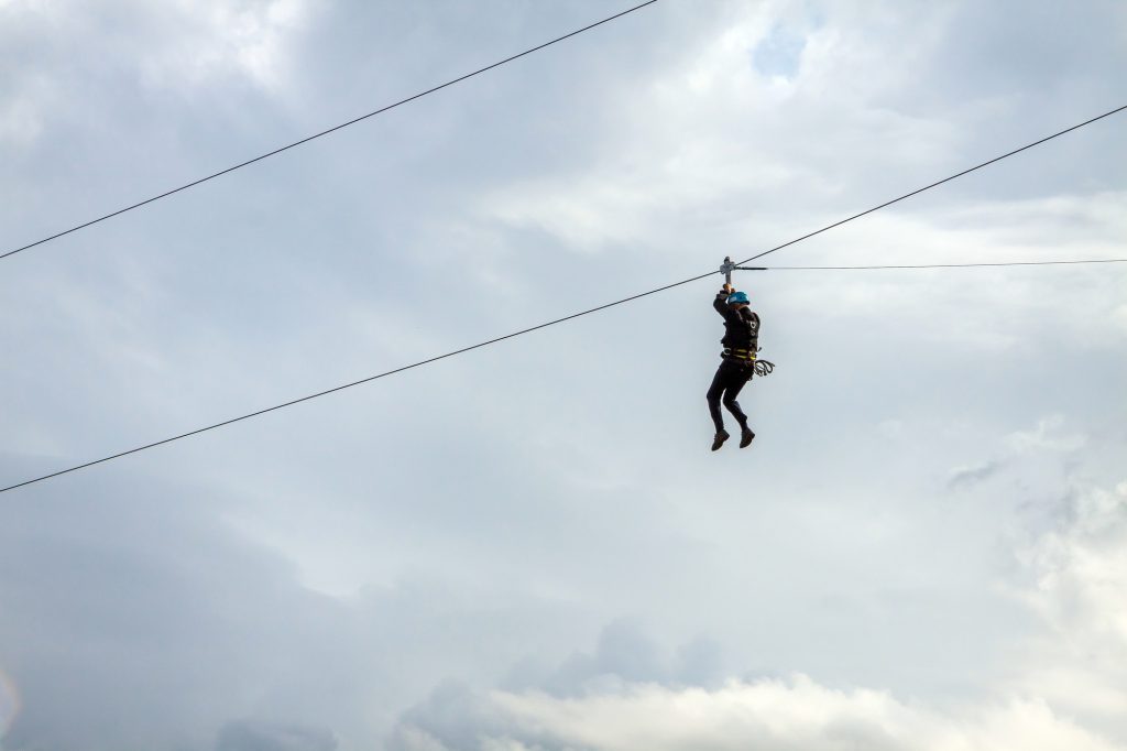 A person hanging from a zipline, against the clouds.