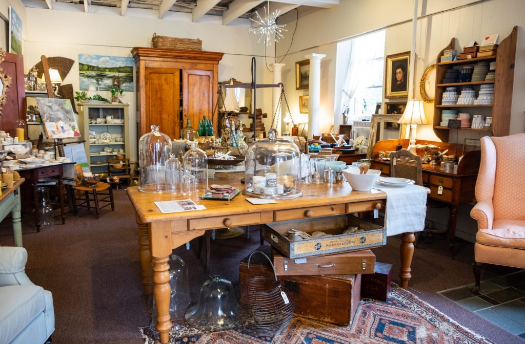 An antique shop filled with piles upon piles of treasures, like glass domes, candles, plates, framed paintings, and trinkets.