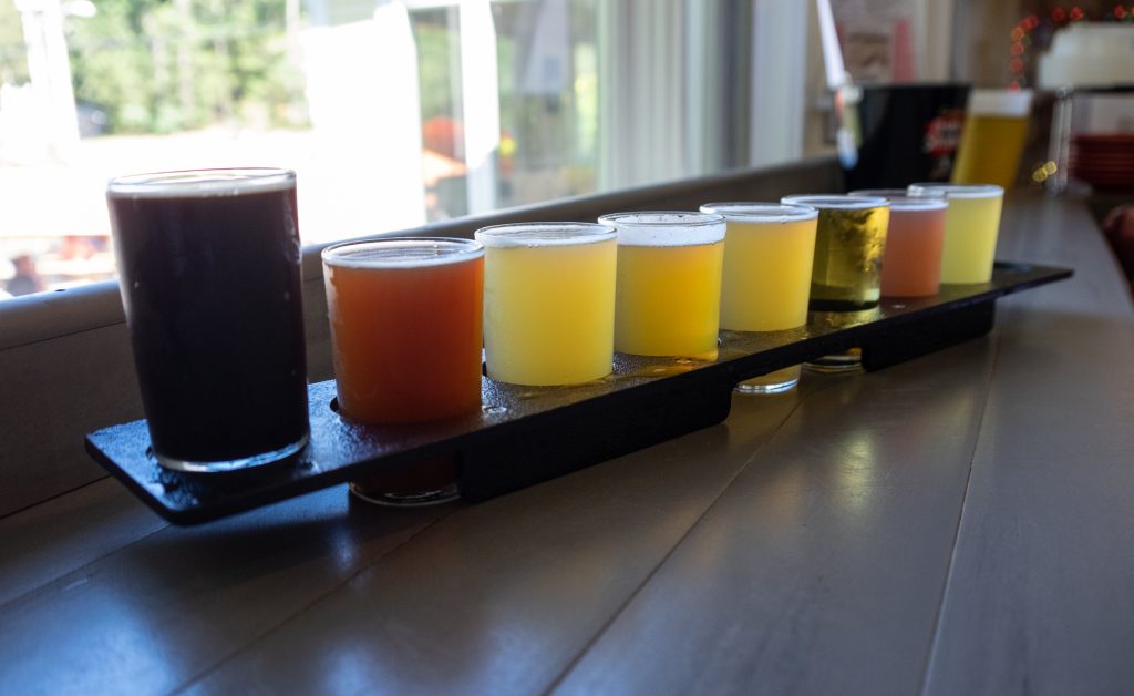 A huge wooden sampler containing eight different small beers of different colors from dark brown to gold.