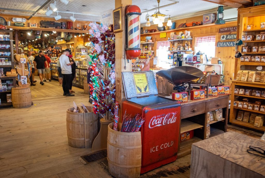 A busy general store with lots of products on the shelves, plus an old-fashioned barbershop pole and antique Coca-Cola cooler.