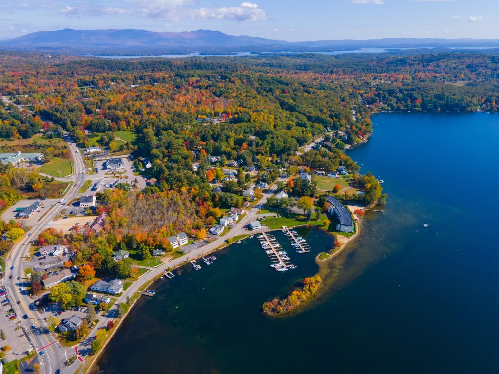 An aerial view of Center Harbor on a fall day, lots of orange and red trees, small houses, and half a dozen boats docked off a pier on the shore.