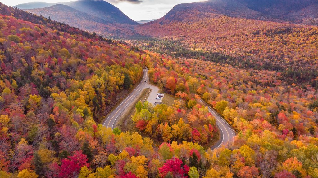 A road winding through a mountainous landscape topped with red, orange, and yellow trees.