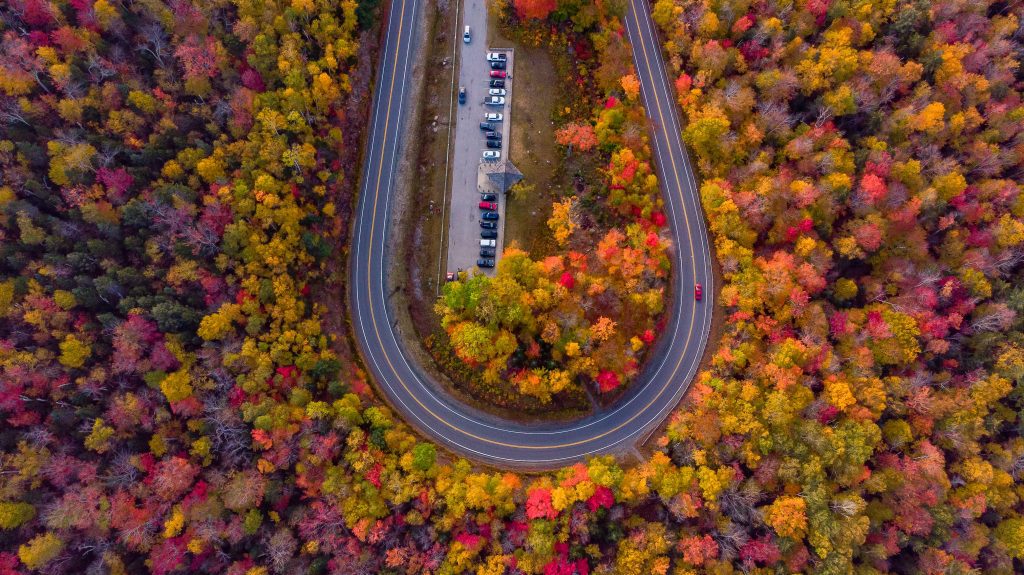 An aerial shot of a highway looping through a landscape of bright red, orange, and yellow trees.