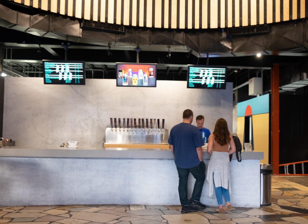 Two people standing by the gray cement counter in a modern, cavernous brewery.