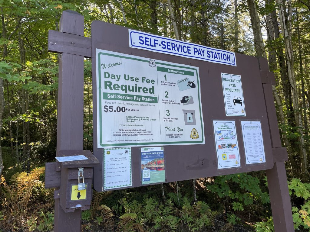 A sign reading Self-Service Pay Station and directions for paying the $5 daily parking fee in cash in an envelope.