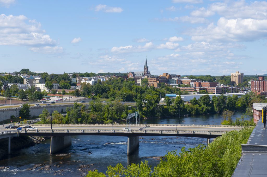 A highway bridge over the rushing Merrimack River, and buildings including a church steeple in the far background.