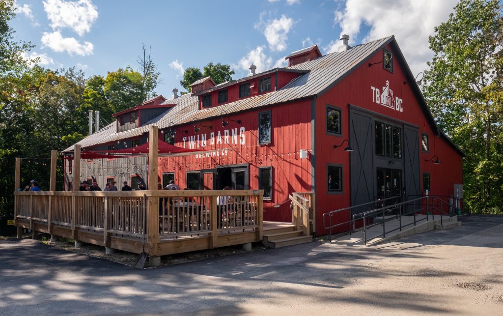 An old-fashioned red barn brewery with an attached wooden deck.