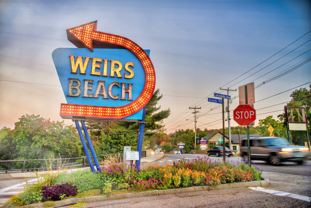 A large neon sign reading "Weirs Beach" with a curving arrow around it.