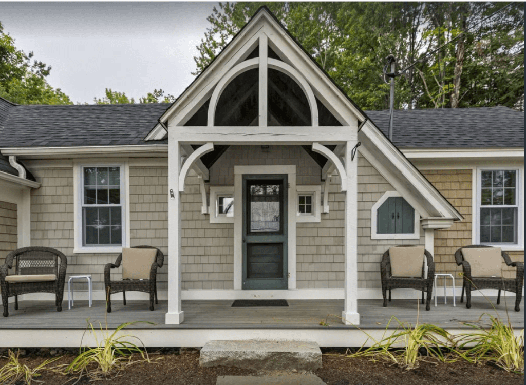 View of a front porch of a tan cottage with gray roof and white accents