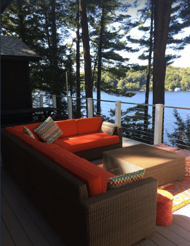 A brown outdoor couch with orange cushions on a deck overlooking the lake
