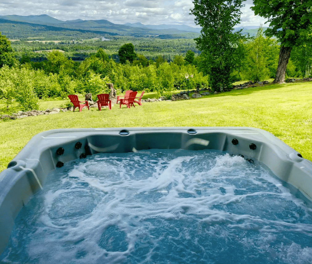 A hot tub on green grass with mountains and a blue sky in the distance