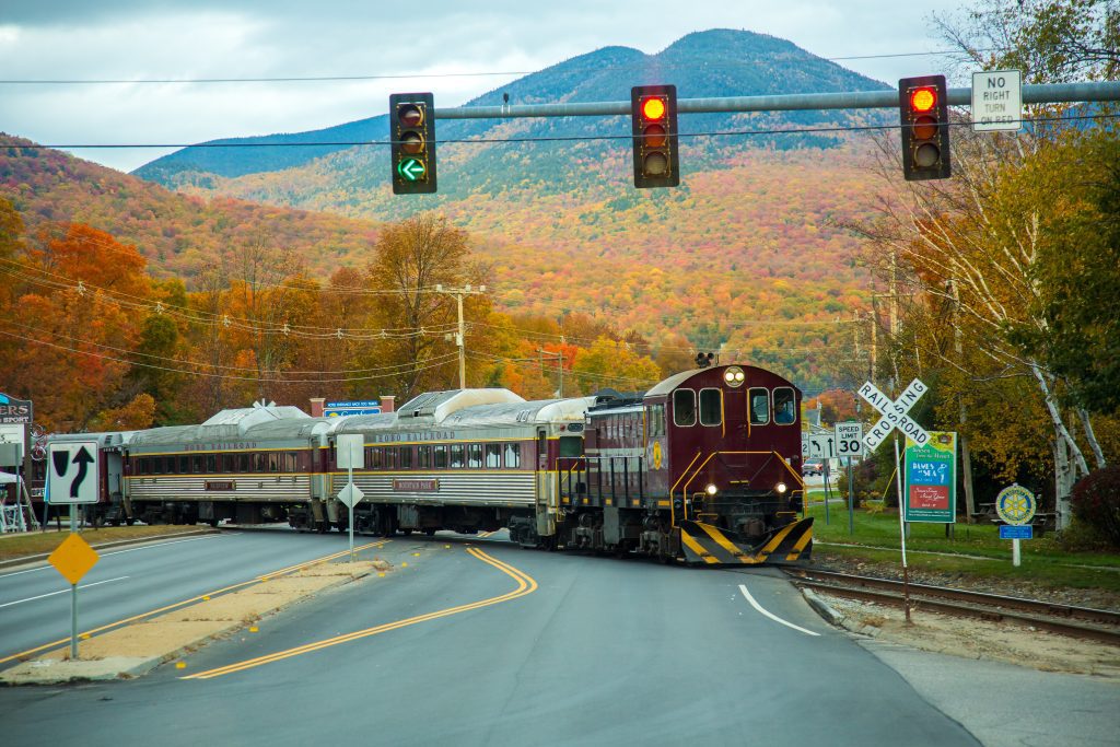 An old-fashioned train driving through a town with mountains in the background.