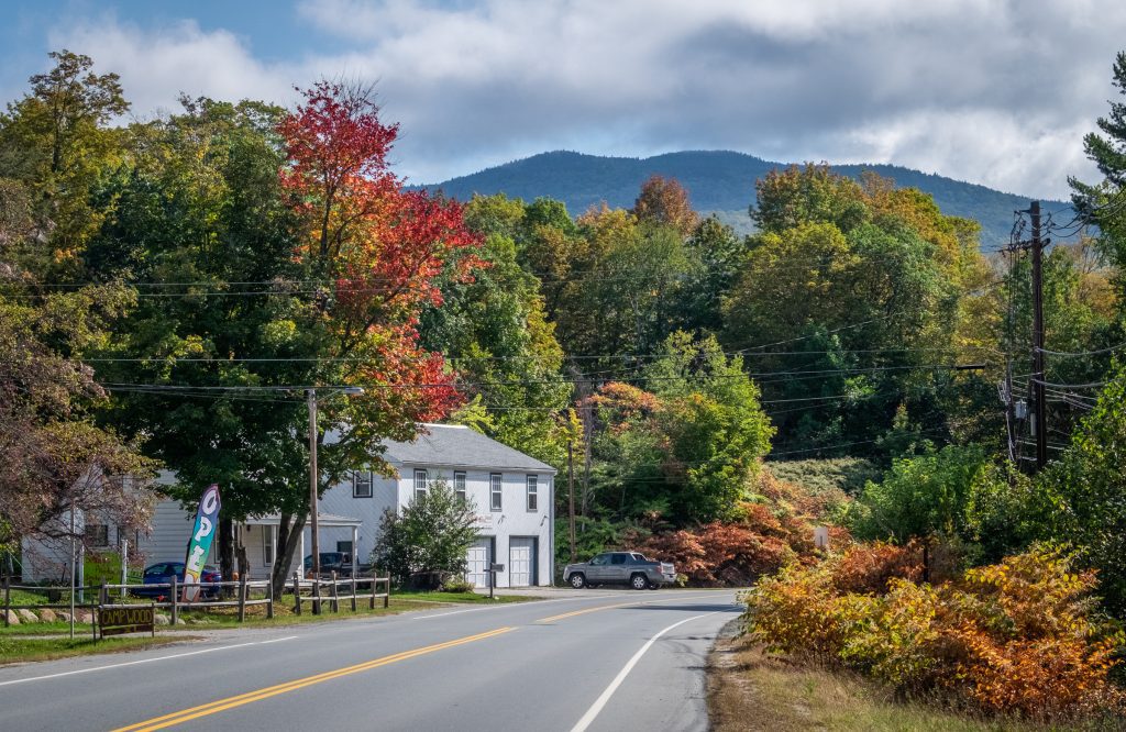 A road through the mountains of New Hampshire with wooded homes and trees beginning to turn red.