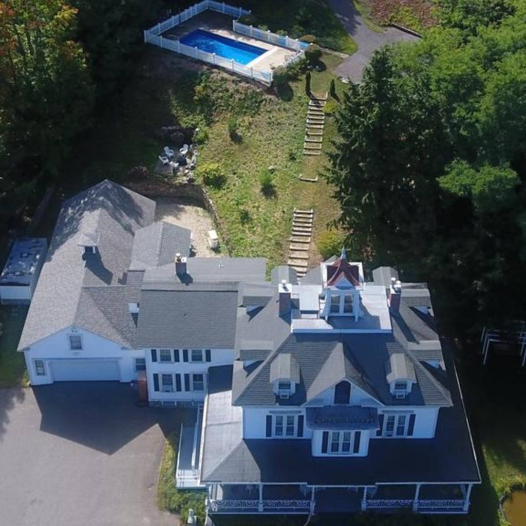 Aerial view of a three story white mansion with a big yard and a pool