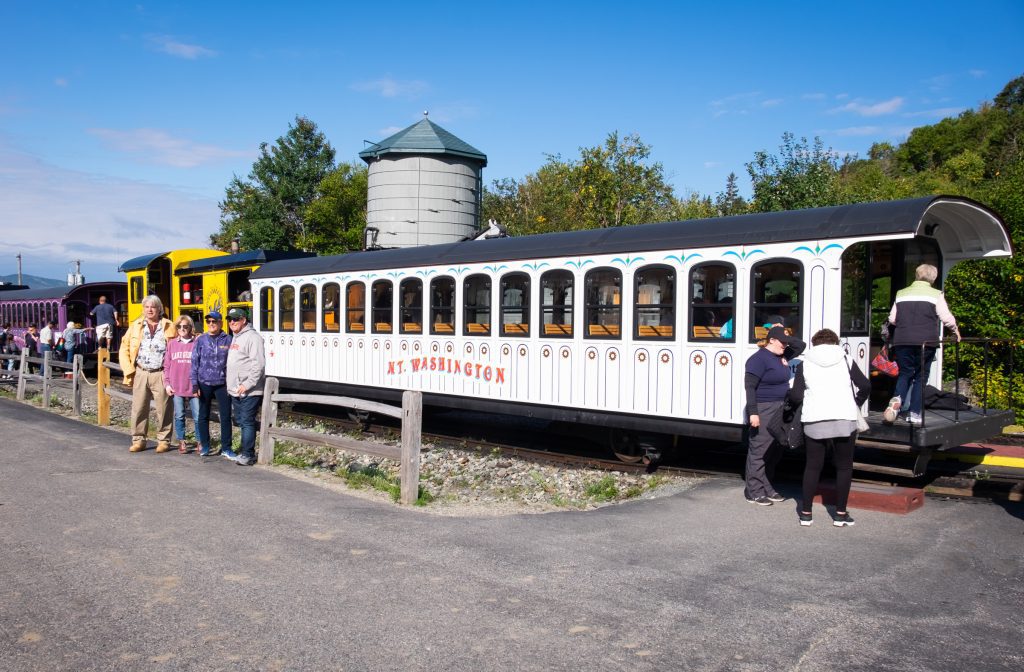 People taking photos in front of a white train car labeled Mt. Washington.