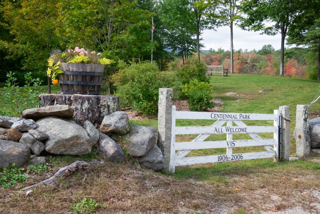 A white picket fence door on a rock wall, leading to a grassy park.