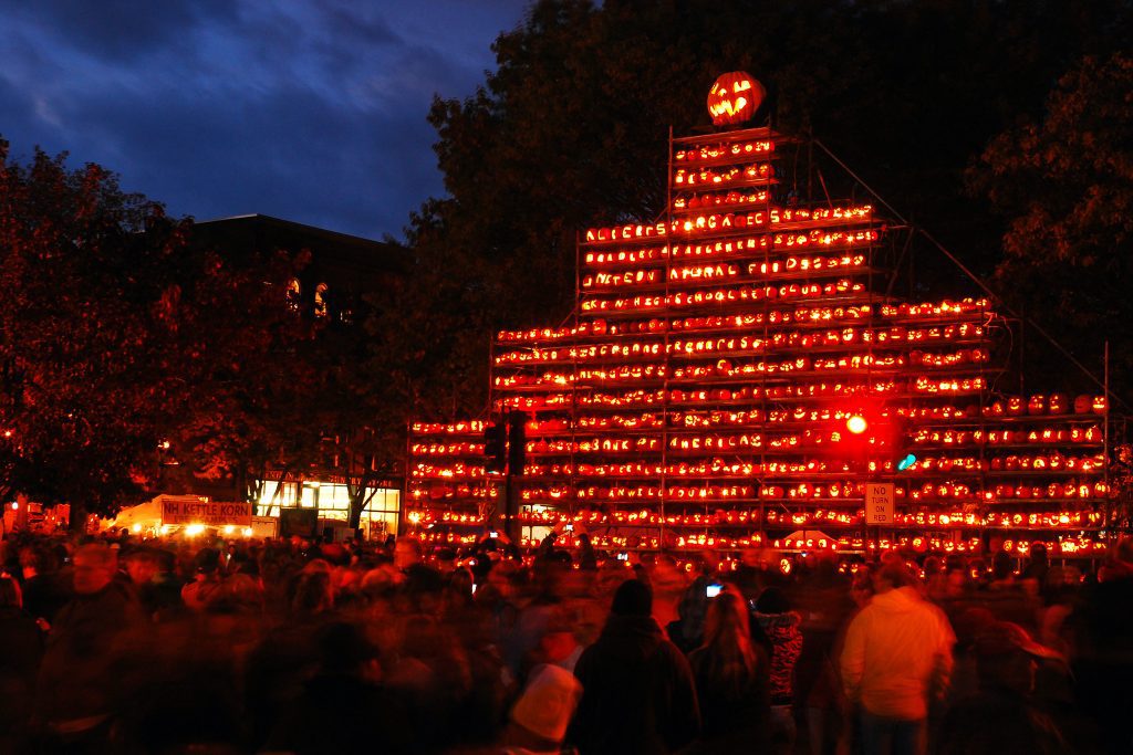 A giant tower of jack o'lanterns lit up at night in front of a crowd.