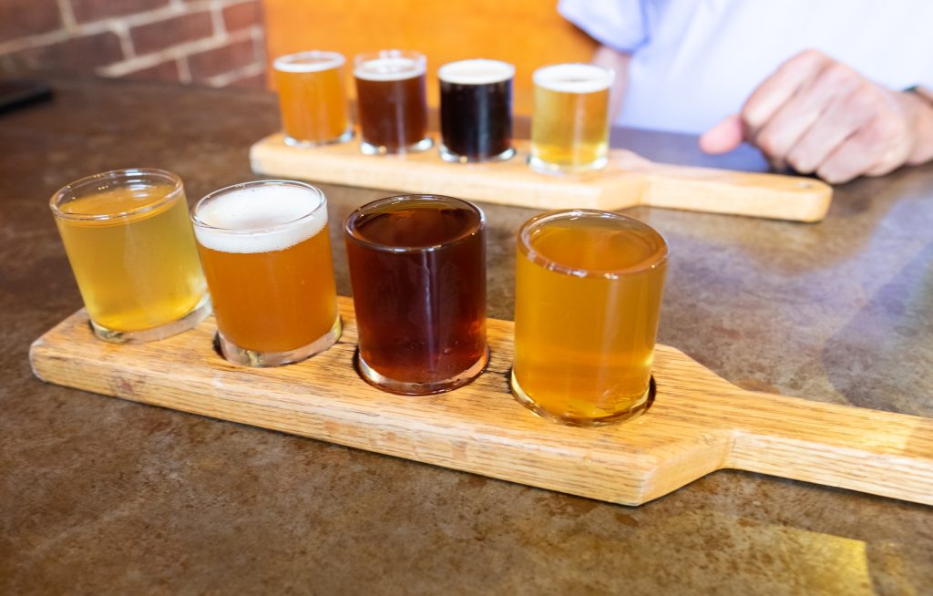 Two wooden paddles with four small glasses of different colored beers on them.