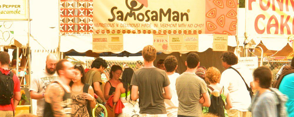 A crowd of students standing in front of a Samosa Man stall at a fair.