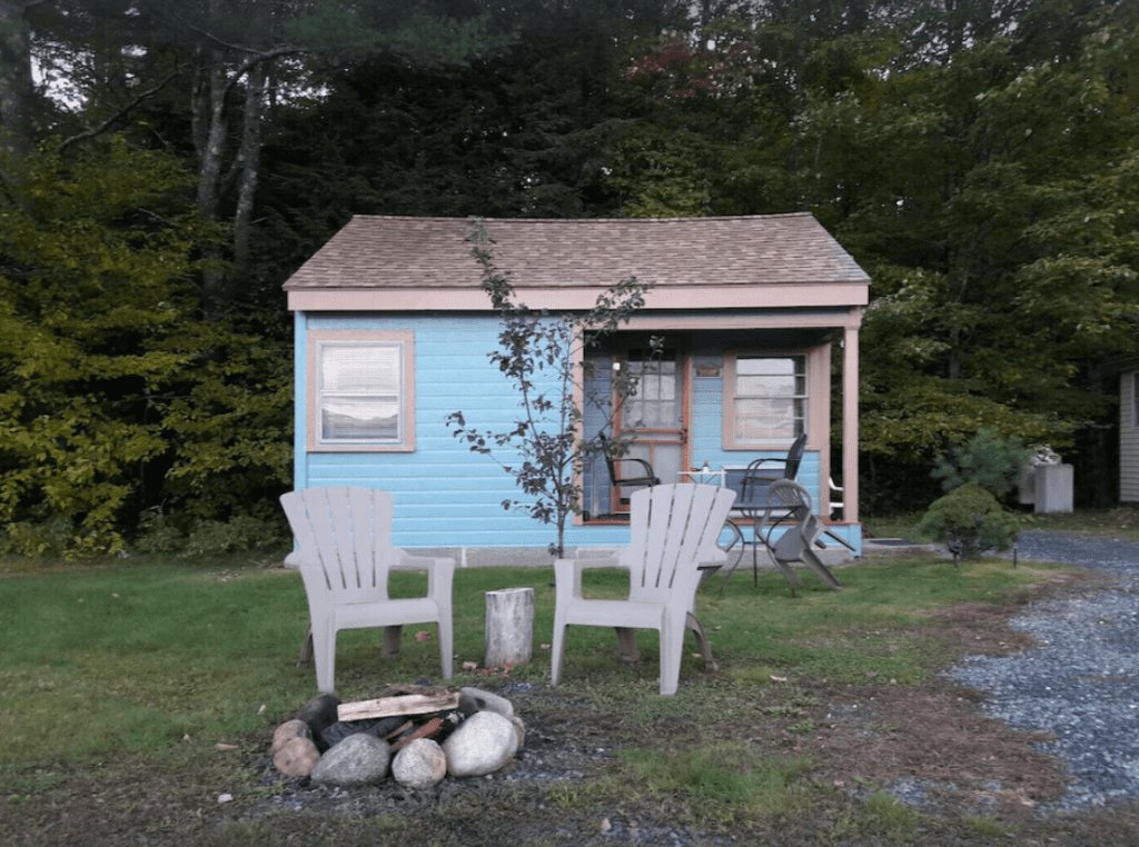 A small blue cabin with adirondack chairs in front