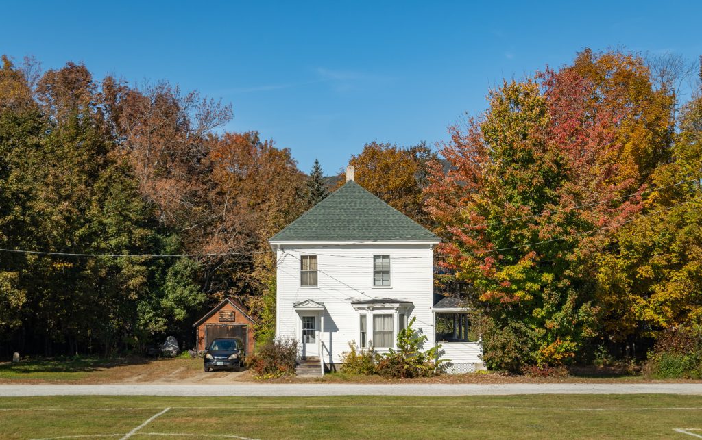 A small white cottage set among green trees starting to turn red.