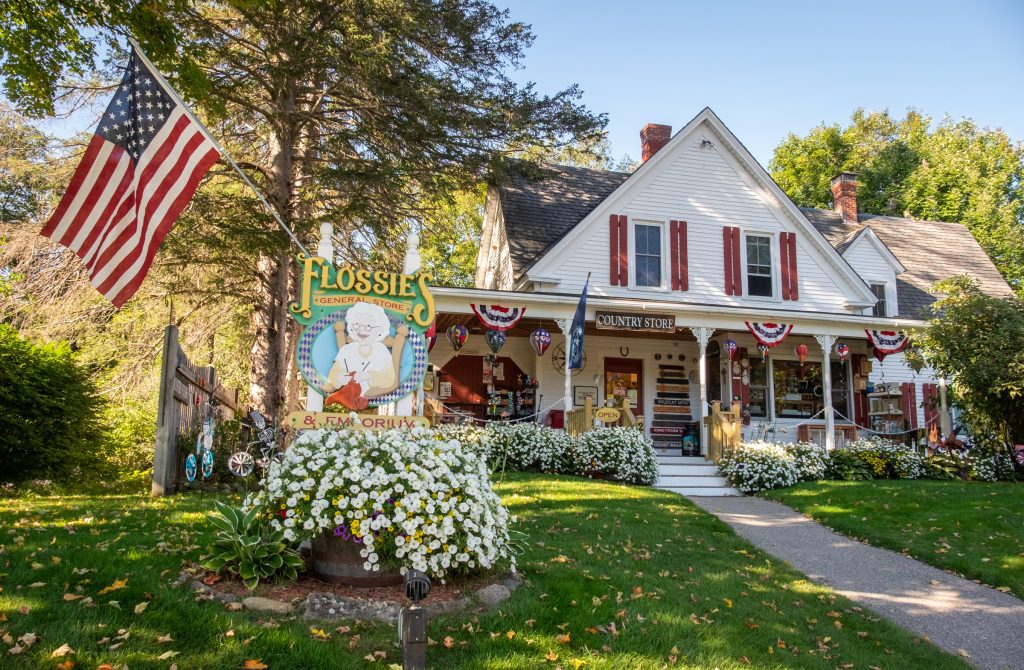 A house with a covered porch filled with flowers, signs, American flags, and a sign reading "Flossie's".