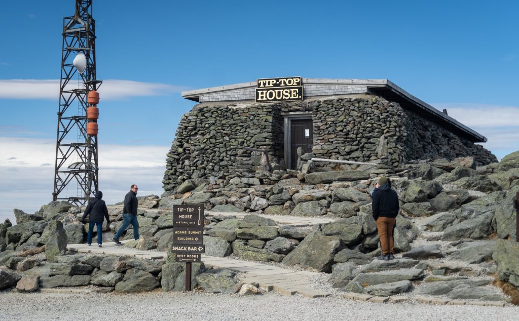 A stone building reading "Tip Top House" next to a tall electrical tower on the mountain summit.