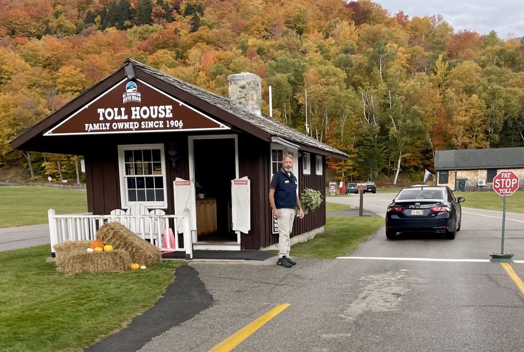A small wooden toll house with a man waiting outside to let cars through.