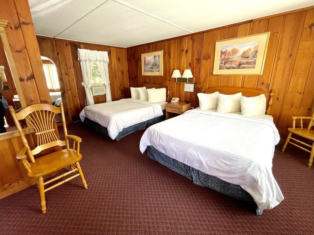 A wood-paneled motel room with two fluffy queen beds.