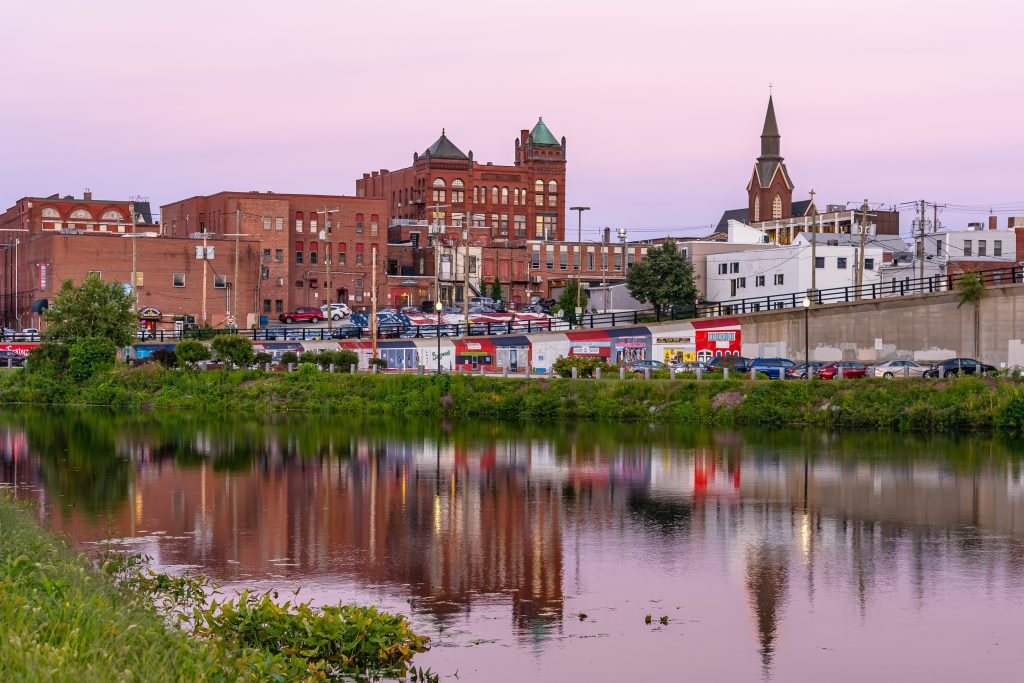 Former mill buildings along a river underneath a pink and purple sunset.