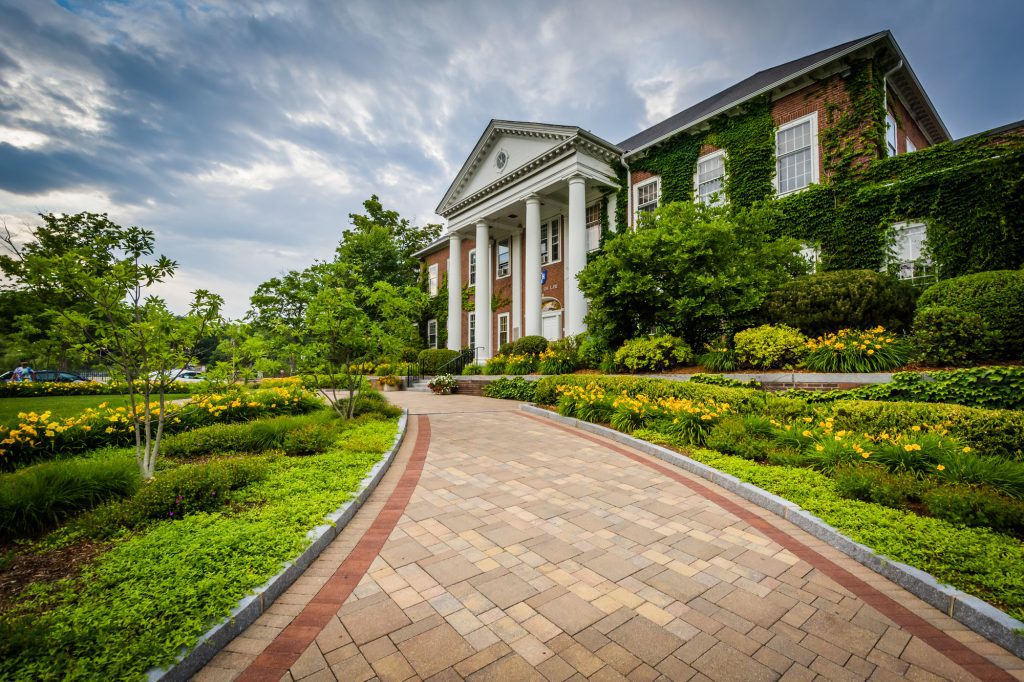 A brick building with tall white columns in front of a well manicured lawn.