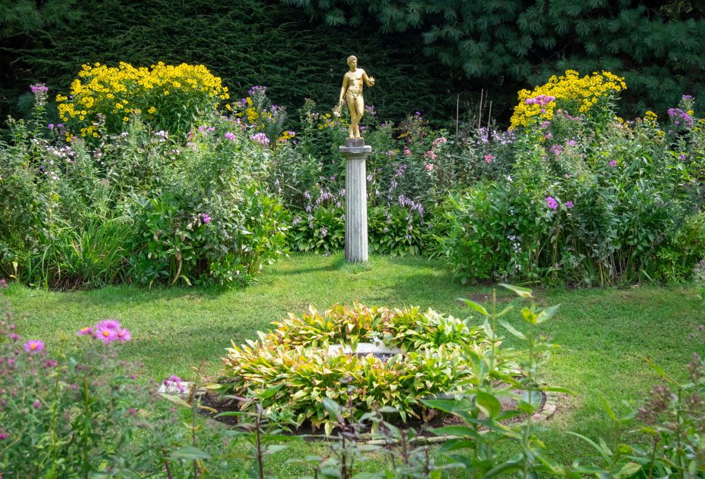 Flower gardens with a small gold state of a man standing up on top of a column.