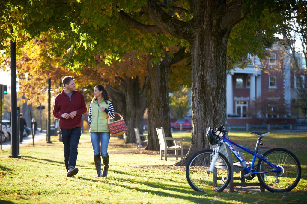 A couple walking along the grass on a college campus underneath fall trees.